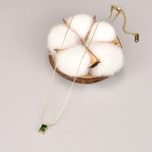 Macro view of a gold square green zircon necklace draped on cotton and wood