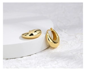 Detailed close-up of thick gold-plated teardrop earrings on a white display stand