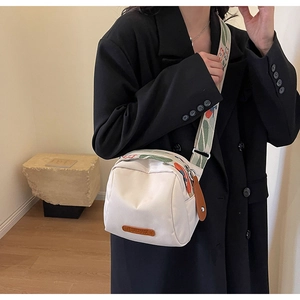 On-body view of a white nylon crossbody bag with printed strap and brown logo patch
