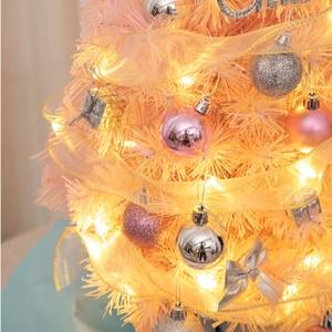 Close-up of pink and gold mini Christmas tree with silver baubles and warm LED lights