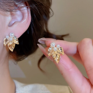 Gros plan de boucles d'oreilles feuilles dorées avec perles blanches et strass brillants