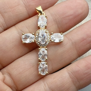 Macro shot of gold cross pendant with oval cubic zirconia held in hand for scale