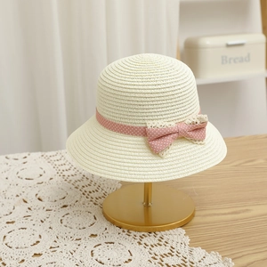 Detail of children straw sun hat featuring a sweet pink polka dot bow on creamy woven texture