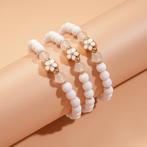 Close-up of three-piece beaded bracelet set featuring white enamel flower charms and beads
