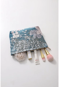 Detail of dark blue floral jacquard makeup bag with gold zipper and beauty tools