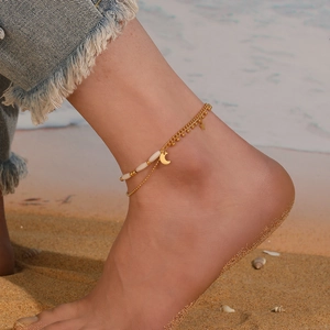 Detail of gold double-layer anklet with moon and star charms worn on beach ankle