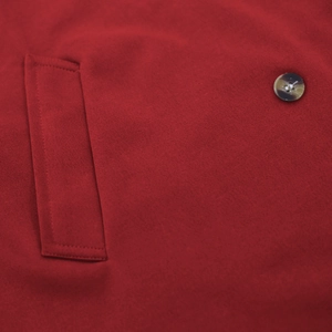 Detail of red knitted coat showing textured fabric pocket and decorative button closure