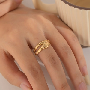 Detail of gold snake-shaped ring with diamond texture worn on the index finger