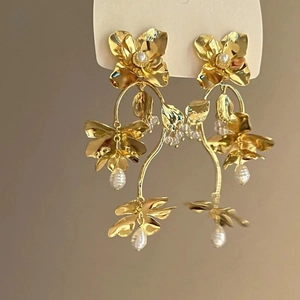 Detail of gold floral tassel earrings featuring triple-layered petals and pearl accents