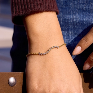 Detailed view of 18K gold wave chain bracelet with white cubic zirconia on a model wrist