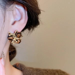 Close-up of a model wearing a gold flower earring with tiger eye stone bead accents