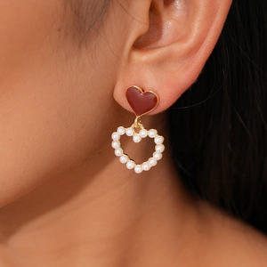 Detail of elegant red heart enamel earrings with pearls worn by a model