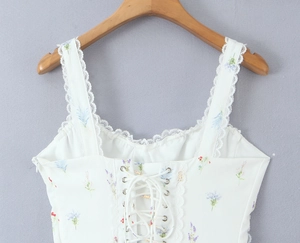 Dettaglio del top bianco a fiori con pizzo, lacci delicati e trama del tessuto intrecciato