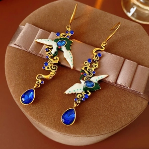 Detailed view of vintage gold crane earrings with enamel and blue crystals on a velvet box