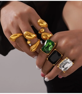 Detail of gold geometric rings featuring emerald, black, and clear rectangle cut crystals