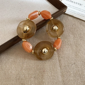 Detailed view of irregular brown and orange acrylic beads bracelet on burlap background