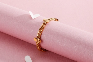 Detail of golden stainless steel bracelet with pineapple pendants on pink paper