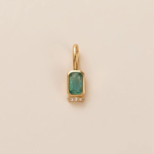 Macro detail of gold birthstone pendant with emerald-cut green stone and clear crystal accents