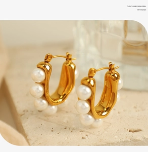 Macro view of dainty gold U-shaped earrings with white round pearls on stone background