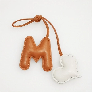 Detail of leather letter M and white heart charm with litchi grain and hand stitching