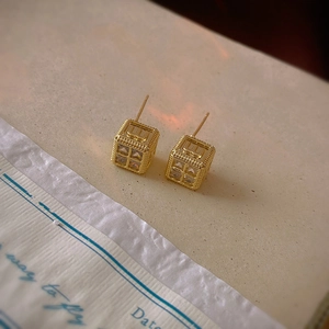 Macro shot of gold square stud earrings with zircon inlay and embossed letter details