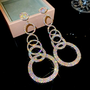 Macro shot of silver drop earrings with colorful rhinestones on a dark mirrored surface