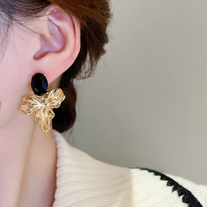 Detail of a gold pleated flower earring with a black oval crystal worn by a model