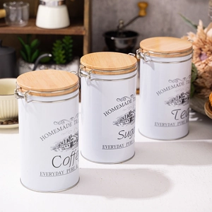 Three white kitchen canisters for coffee sugar and tea with wooden lids in a kitchen setting