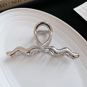 Detailed close-up of a silver metallic wave-shaped hair claw clip on a white plate