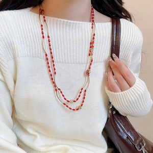 Detail of double-layer beaded necklace featuring red oval stones and gold floral accents