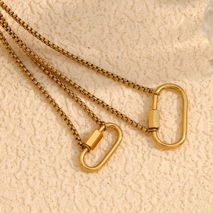 Detail of 18K gold-plated box chain with oval screw lock carabiner on textured surface