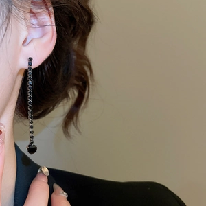 Close-up of elegant long black tassel earrings with faceted stones worn by a model