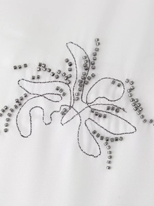 Detail of grey metallic beads and intricate black embroidery on white fabric