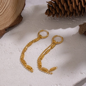 Gold tassels earrings with geometric rings and long bead chains on a stone background