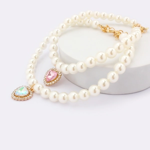 Close-up of pearl pet necklaces with pink and white crystal heart pendants and gold hardware