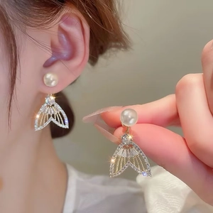 Détail de boucles d'oreilles queue de sirène dorées avec cristaux et perles