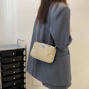 Detail view of beige corduroy crossbody bag featuring a golden metal chain strap