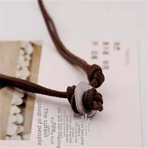 Detailed close-up of brown leather cord knot and retro metal spacer pendant