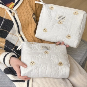 Detail of white quilted cosmetic bag with soft bear embroidery and floral stitching