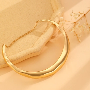Detailed view of a wide gold wavy collar necklace with adjustable chain on a stone tray