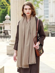 Close-up of a warm beige cashmere-like scarf with fringe detail worn with a brown coat