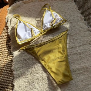 Detailed flat lay of a mustard yellow sequin bikini with sparkling texture and tie straps