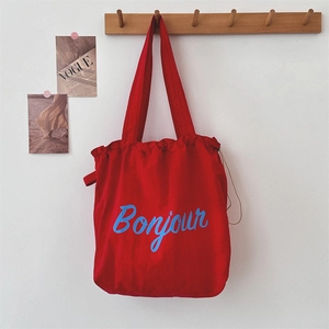 Detailed macro shot of red canvas drawstring tote bag featuring blue Bonjour letter print