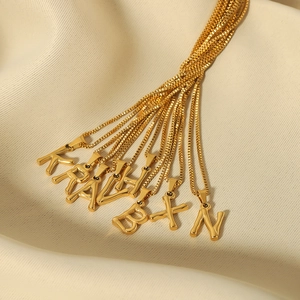 Macro view of 18k gold plated stainless steel letter pendants on a beige fabric background