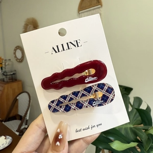 Detail view of wavy red and plaid acetate hair clips on a branded display card
