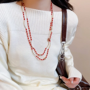 Detail of a double-layered long red beaded necklace with gold accents on a white sweater