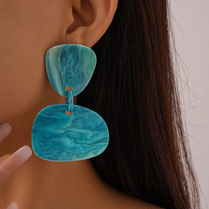 Close-up of oversized irregular resin earrings with teal marble texture on a model