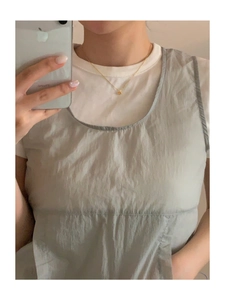 Close-up of minimalist gold heart pendant necklace layered over a white t-shirt