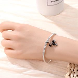 Detailed view of a silver snake chain bracelet with black heart and camera charms on wrist