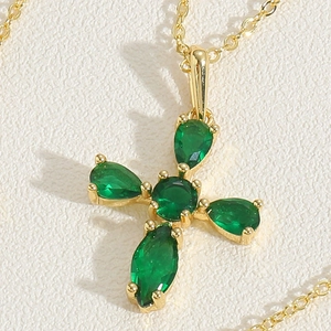 Macro view of gold cross necklace featuring pear-cut green zircon stones on leather